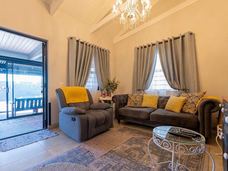 A bright living room featuring a vaulted ceiling with exposed beams, tiled flooring, and a sliding glass door providing access to an outdoor patio area.
