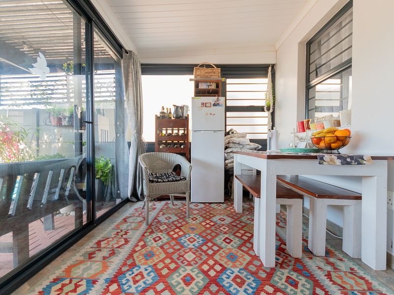 A bright, enclosed patio area featuring large sliding glass doors, timber ceiling, and louvre windows, providing a versatile space for dining or relaxation.