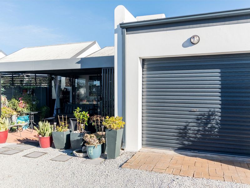 Front view of the property featuring a secure roller garage door and an adjacent covered patio area with gravel landscaping.