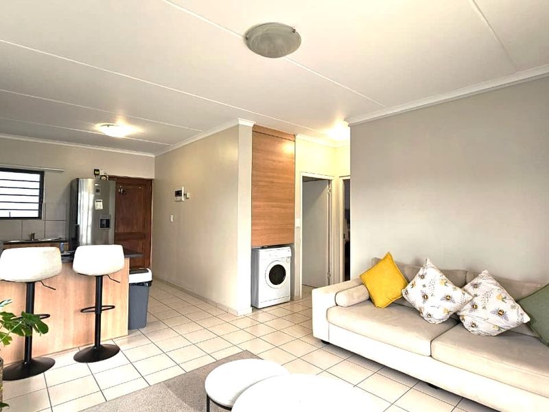 Open-plan living area featuring a functional kitchen with breakfast bar, tiled flooring, and a convenient built-in laundry cupboard.