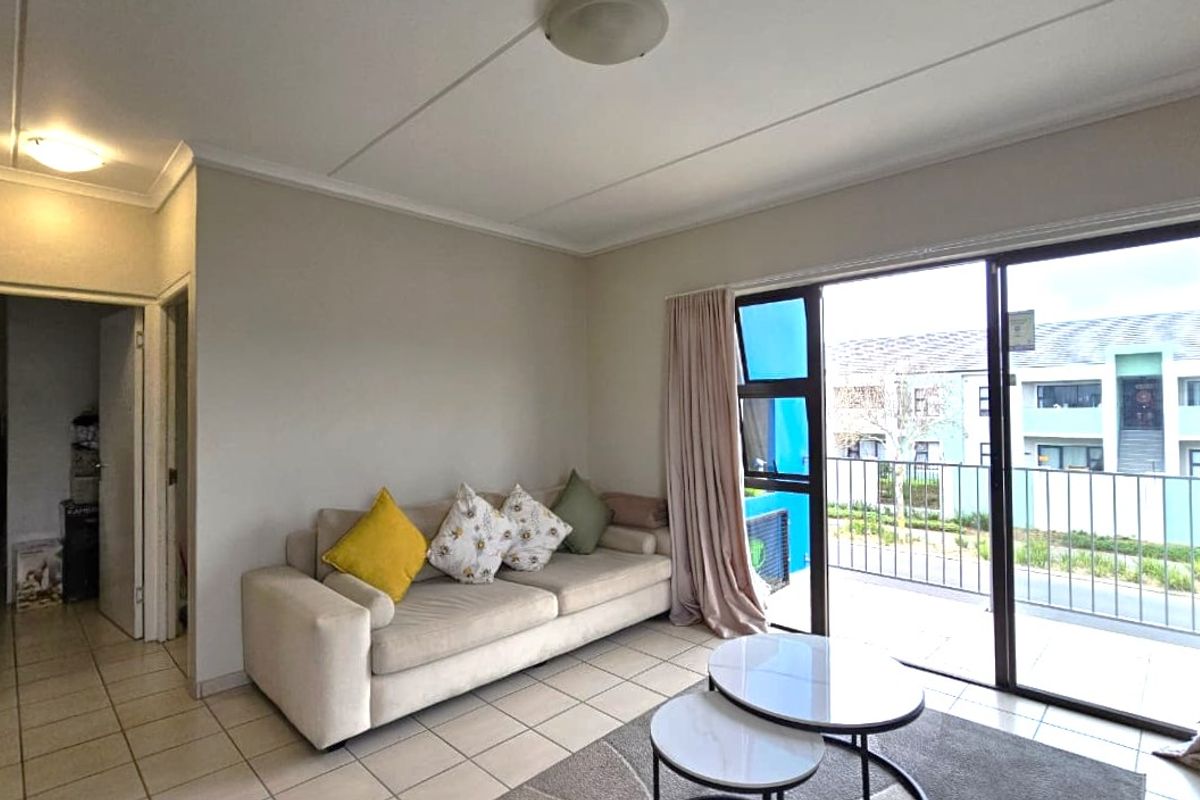 A bright living room featuring tiled flooring and a large sliding glass door that provides direct access to an outdoor balcony area.