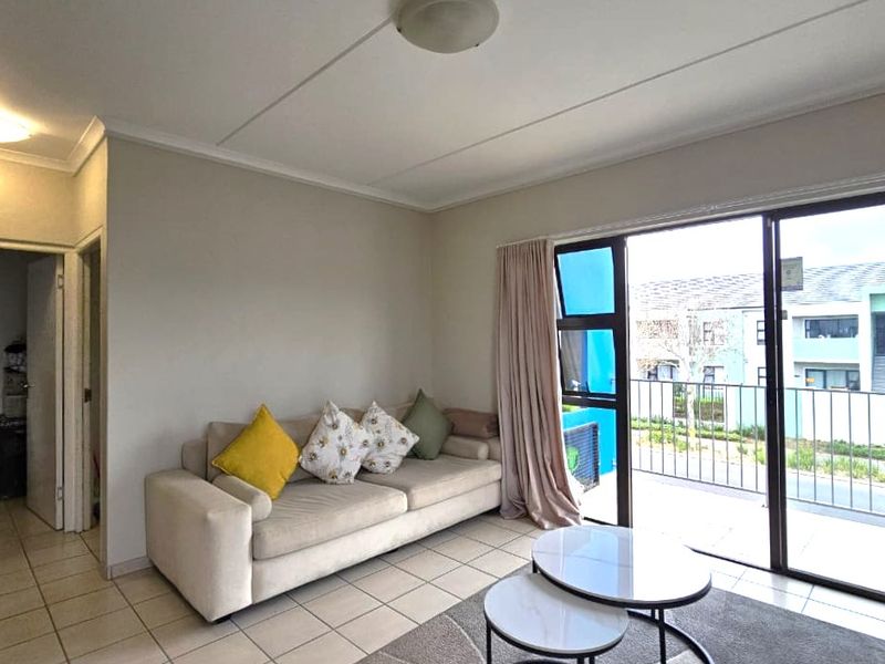 A bright living room featuring tiled flooring and a large sliding glass door that provides direct access to an outdoor balcony area.