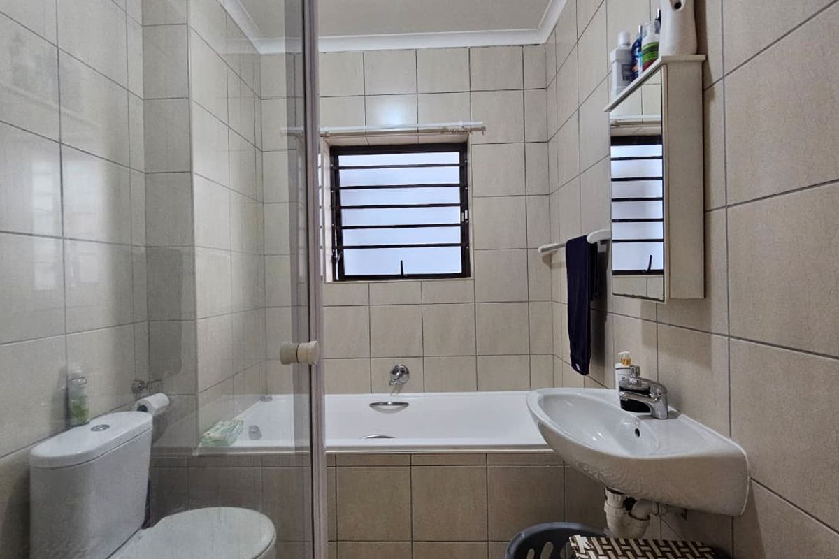 A functional bathroom featuring a built-in bathtub, separate glass shower enclosure, wall-mounted basin, and neutral wall tiling.