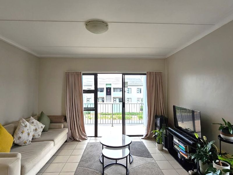 A bright living room featuring tiled flooring and a large sliding glass door providing direct access to an outdoor balcony area.