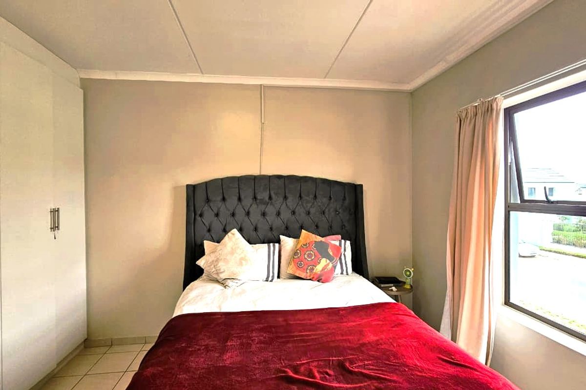 A functional bedroom featuring built-in wardrobes, tiled flooring, and a large window providing natural light.
