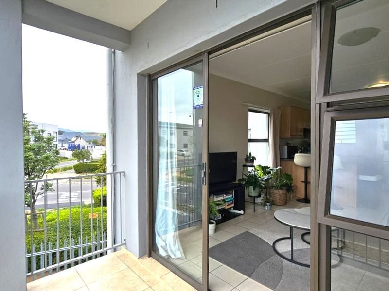 A covered balcony with tiled flooring and a metal balustrade, providing a seamless transition to the interior living area through large sliding glass doors.