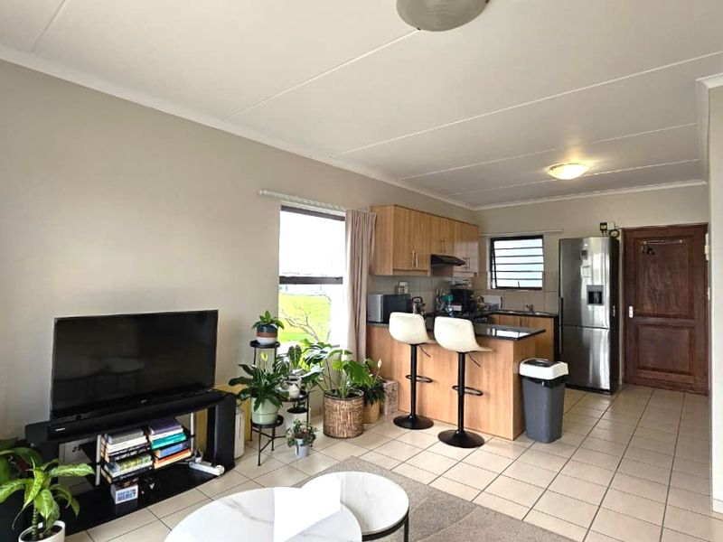 Open-plan living area featuring a functional kitchen with built-in cabinetry, tiled flooring, and direct access to the main entrance.