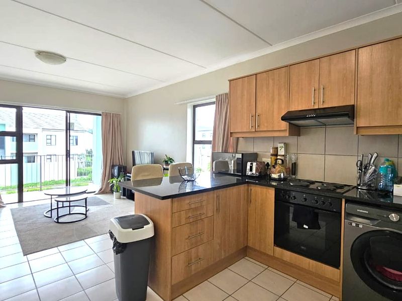 Open-plan living area featuring a functional kitchen with wood-finish cabinetry, granite countertops, and integrated appliances, flowing seamlessly to a balcony through sliding glass doors.
