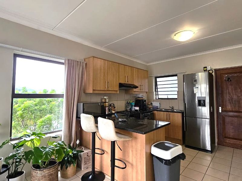 Functional kitchen featuring light wood cabinetry, granite countertops, a breakfast bar, and tiled flooring with natural light from a large window.