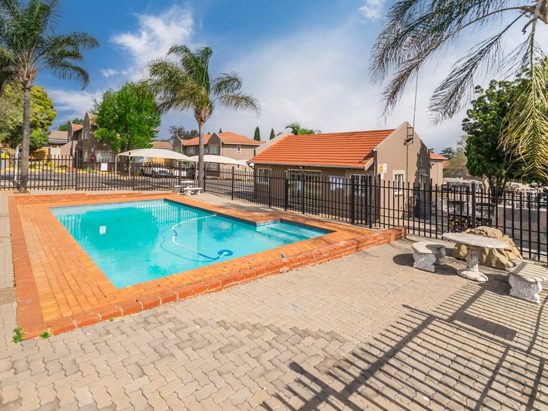 Communal swimming pool area featuring a paved deck, brick coping, and secure metal perimeter fencing within a residential apartment complex.