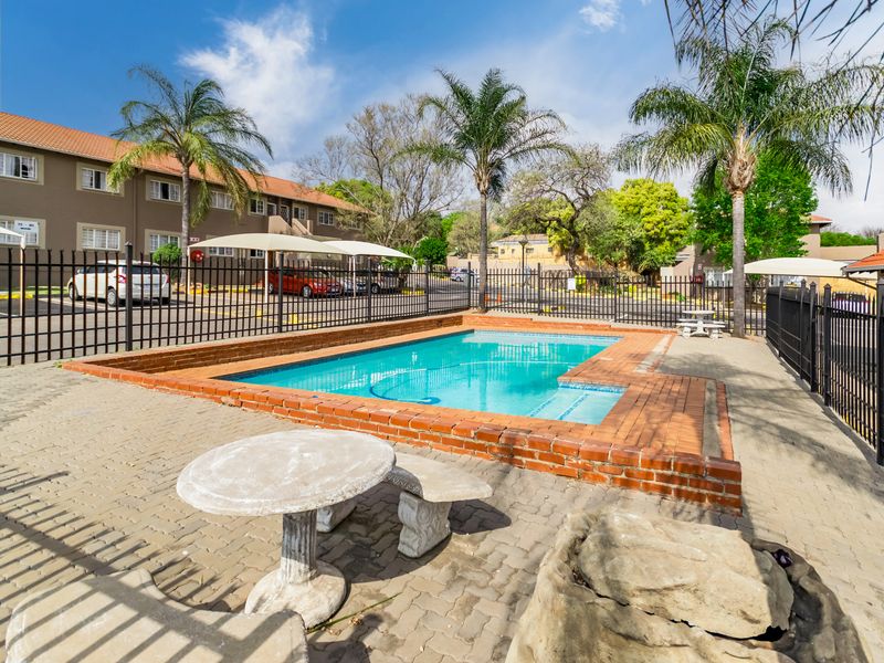 Communal swimming pool area featuring brick coping, paved surround, and secure metal perimeter fencing within the apartment complex grounds.