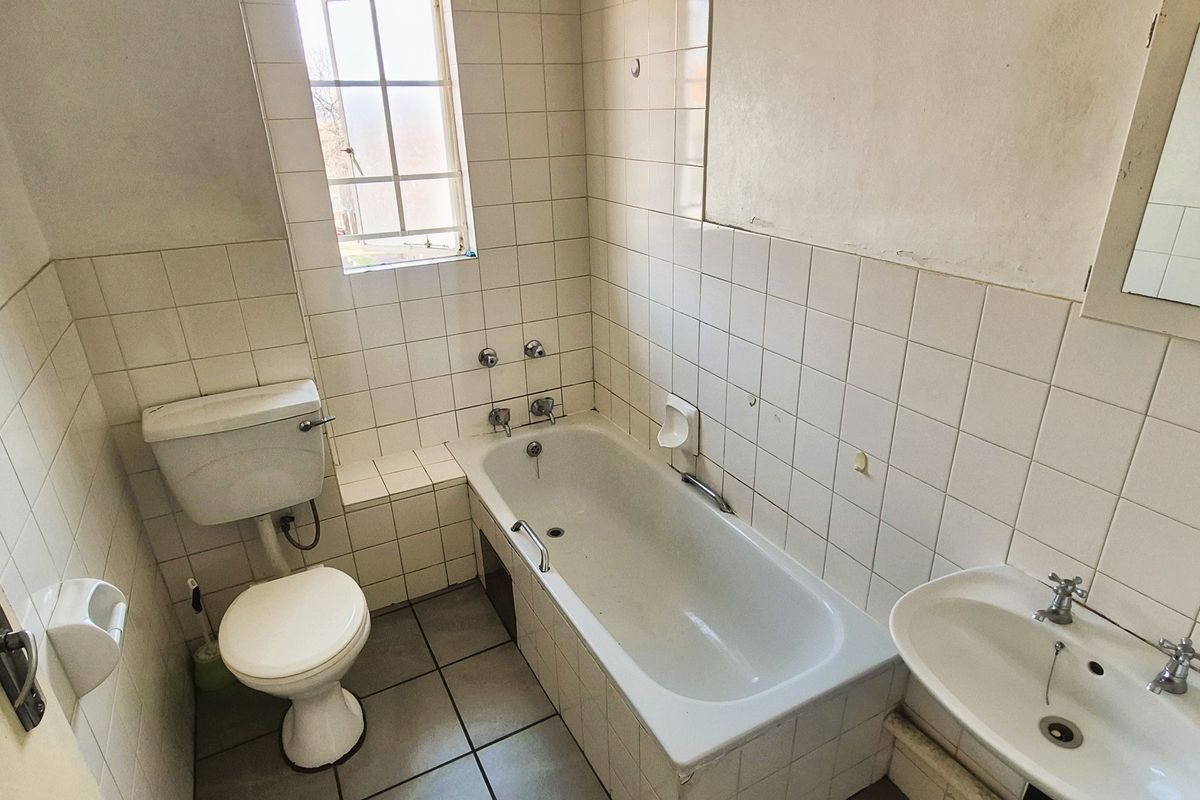 A dated bathroom featuring a standard bathtub, pedestal basin, and toilet with original ceramic tiling throughout.