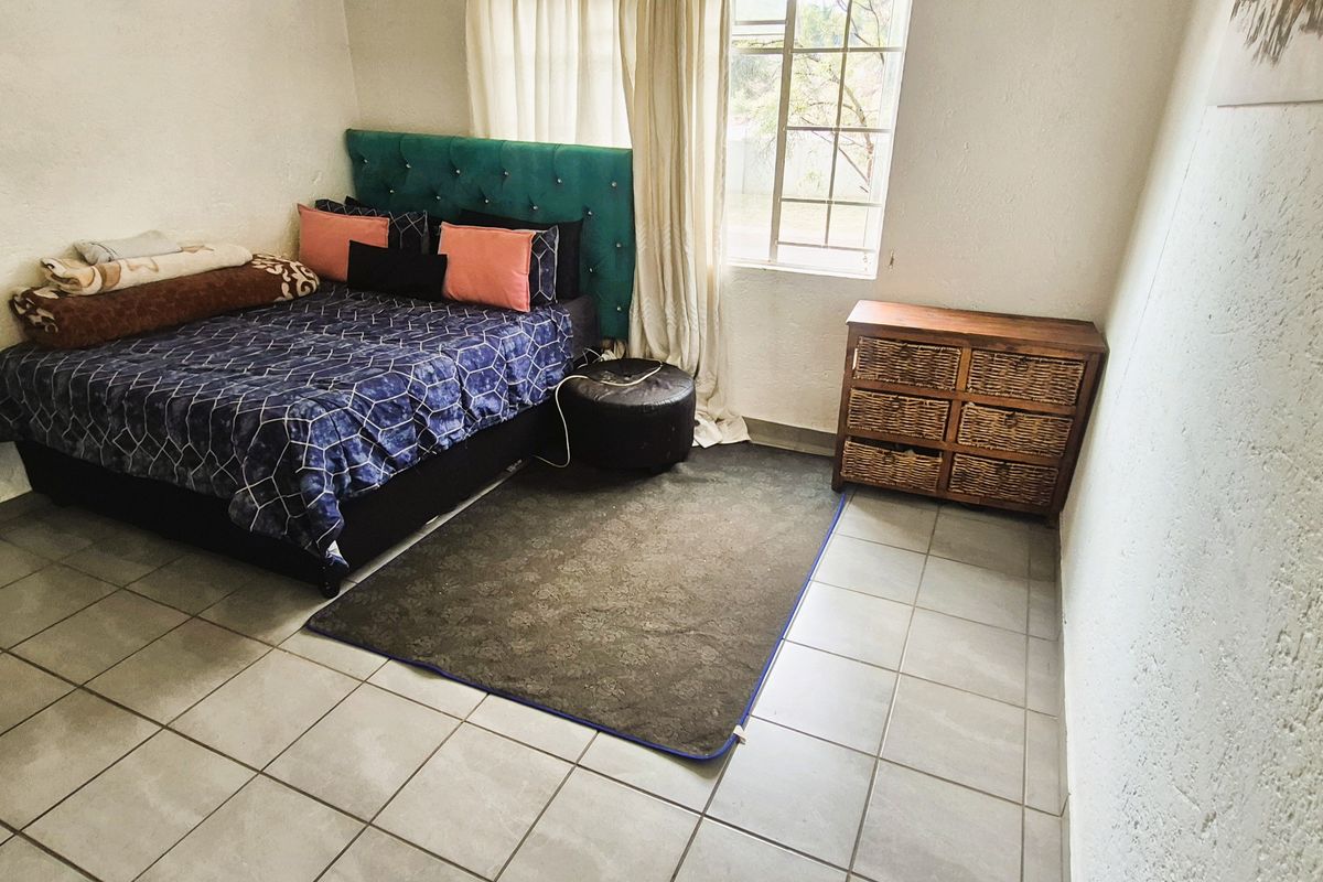 A functional bedroom featuring tiled flooring, textured walls, and a window with security bars, providing a simple and practical living space.
