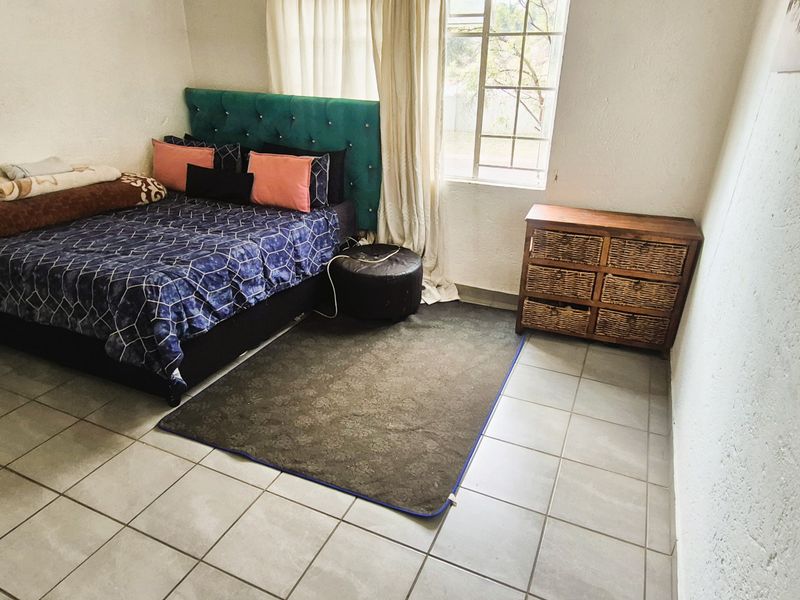 A functional bedroom featuring tiled flooring, textured walls, and a window with security bars, providing a simple and practical living space.