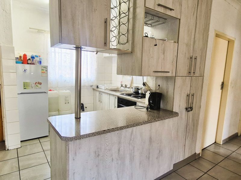 Functional kitchen featuring laminate cabinetry, a breakfast bar, built-in oven, hob, and tiled flooring, providing a practical layout for daily use.