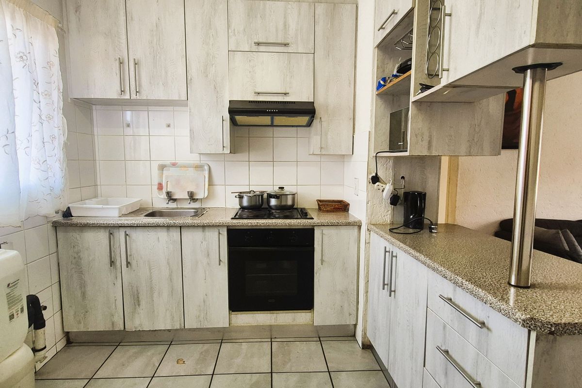 A functional kitchen featuring light wood-grain cabinetry, granite-look laminate countertops, built-in oven and hob, and a breakfast bar overlooking the living area.