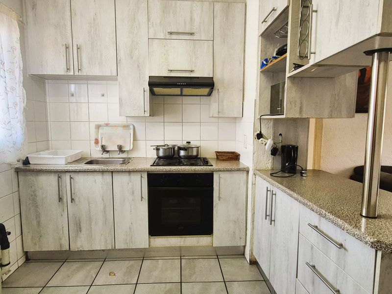A functional kitchen featuring light wood-grain cabinetry, granite-look laminate countertops, built-in oven and hob, and a breakfast bar overlooking the living area.