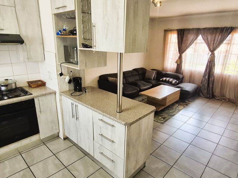 Open-plan kitchen and living area featuring light wood-look cabinetry, tiled flooring, and a functional breakfast counter layout.