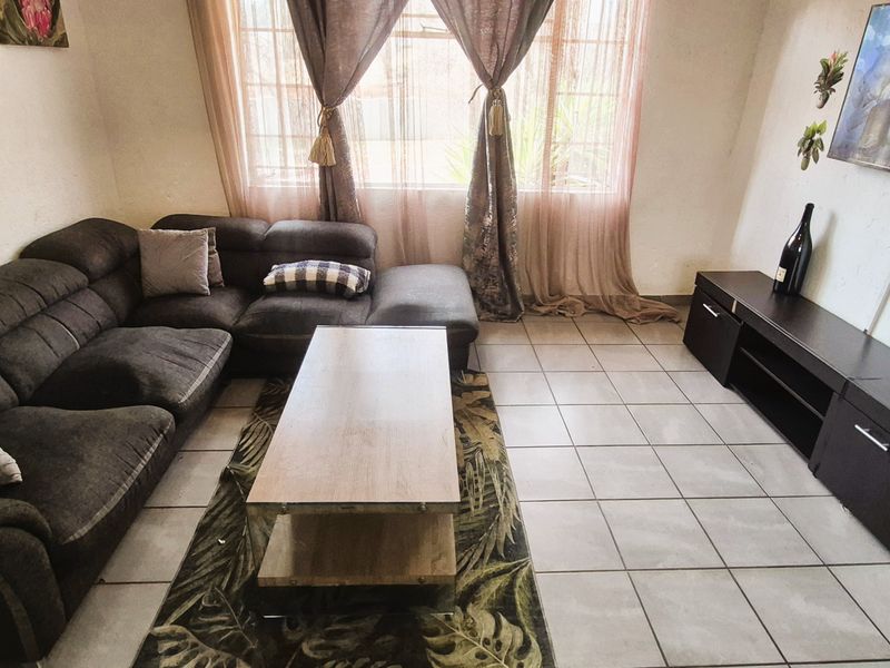 A functional living room featuring neutral tiled flooring and large windows with curtain treatments, providing a comfortable and well-lit space.