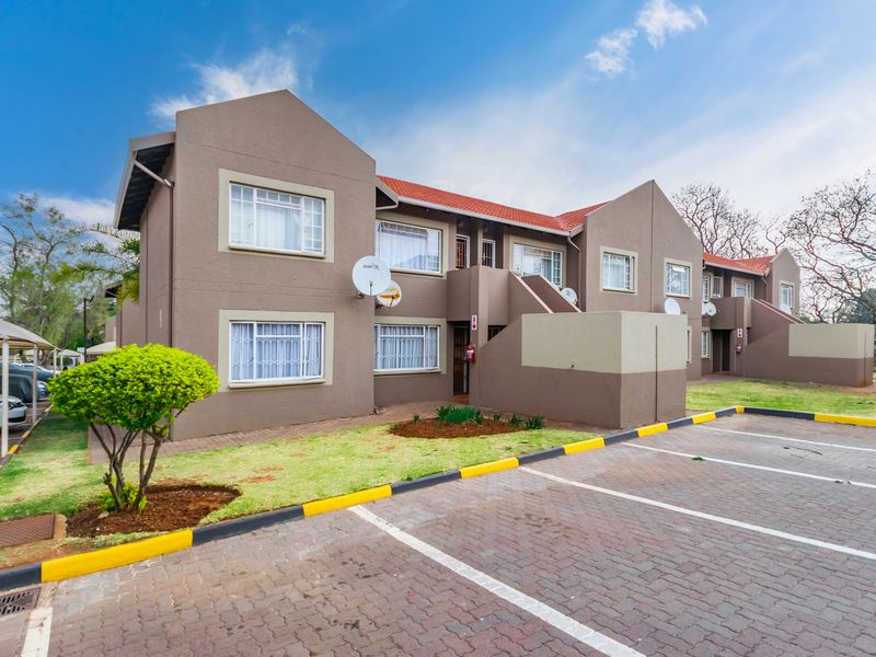 Front elevation of a multi-unit apartment complex featuring paved parking bays, tiled roofing, and well-maintained exterior walls.
