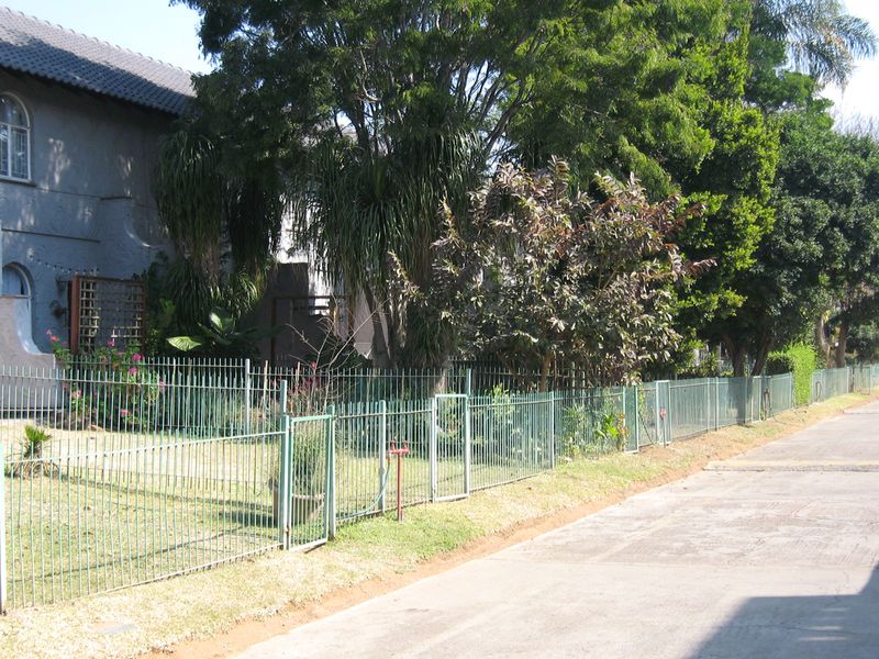 Front exterior view of the townhouse featuring a metal perimeter fence, established garden, and concrete driveway access.