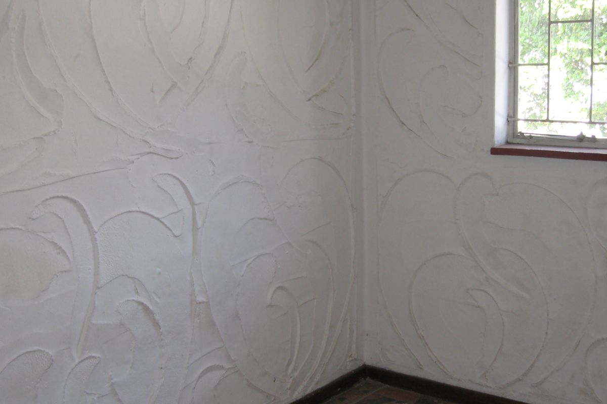An empty room featuring unique textured plaster wall finishes, tiled flooring, and a window fitted with security bars.