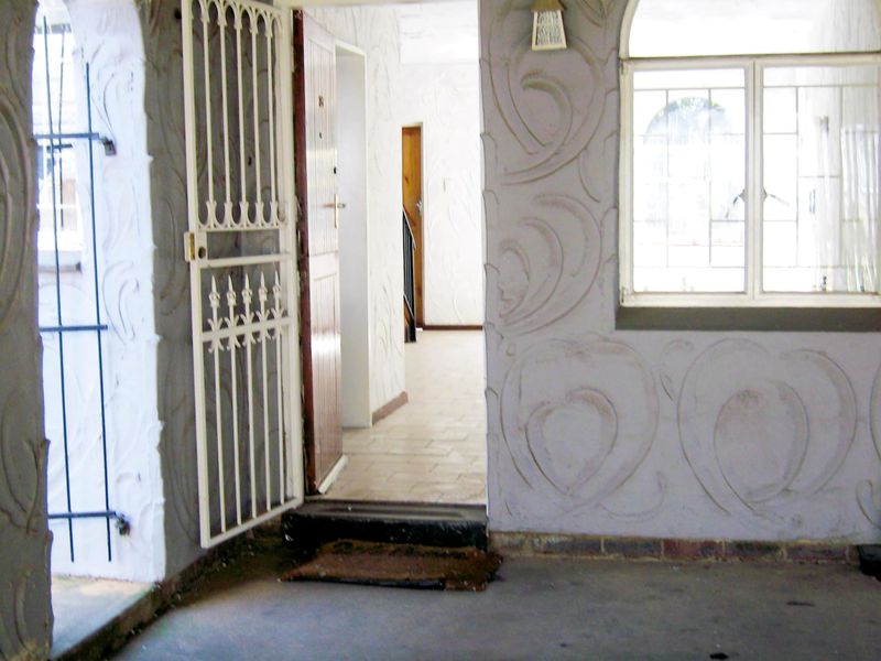 Covered entrance area featuring textured plaster walls, security gate, and tiled flooring leading into the interior of the townhouse.