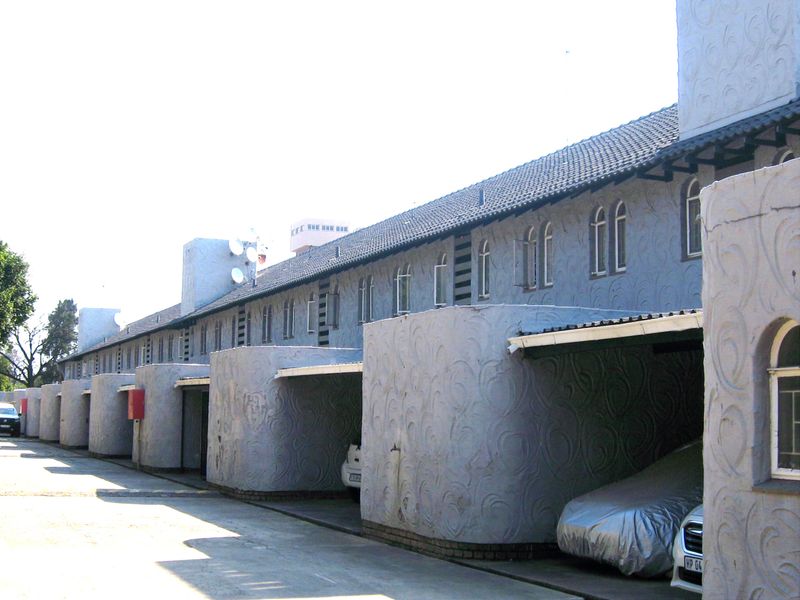 A row of townhouse units featuring covered carports, textured grey facades, and arched window detailing along the exterior elevation.