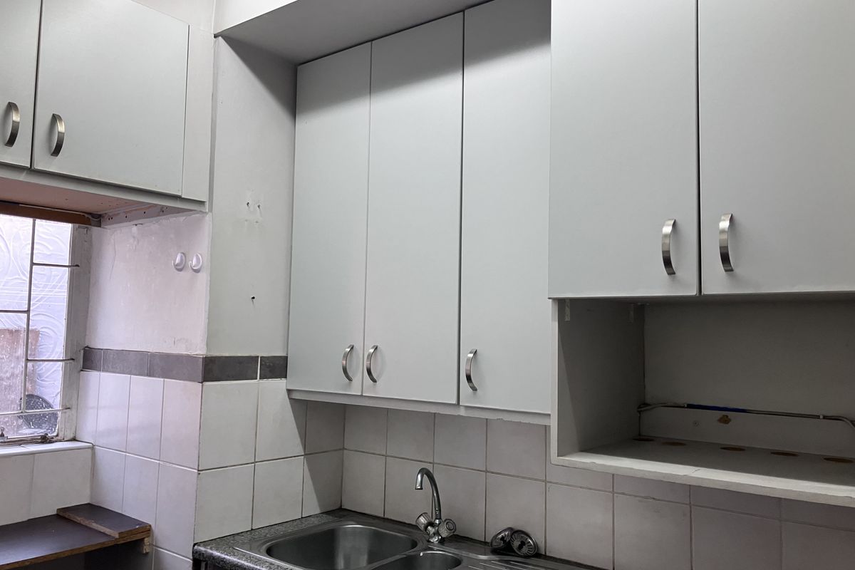 A functional kitchen area featuring built-in cabinetry, a stainless steel double sink, and tiled backsplash, currently vacant and ready for updates.