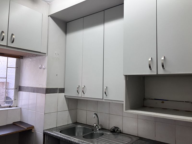 A functional kitchen area featuring built-in cabinetry, a stainless steel double sink, and tiled backsplash, currently vacant and ready for updates.