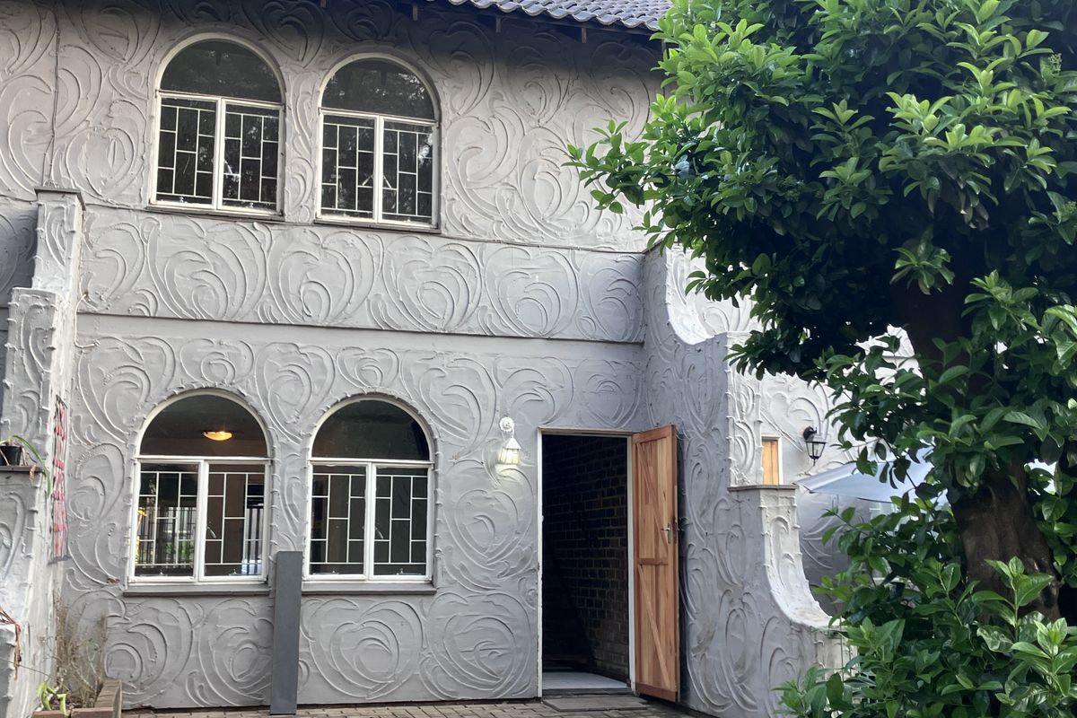 Rear elevation of a two-story townhouse featuring a textured stucco facade, arched windows, and a paved patio area.