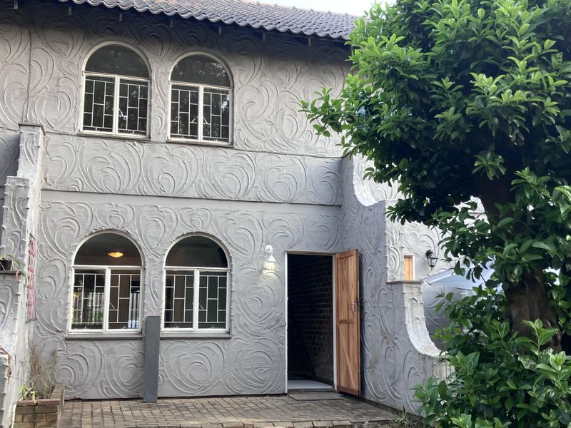 Rear elevation of a two-story townhouse featuring a textured stucco facade, arched windows, and a paved patio area.