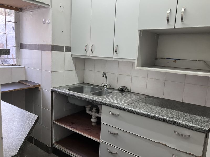 A dated kitchen area featuring built-in cabinetry, a stainless steel sink, and tiled backsplash, currently requiring cosmetic updates and repairs to cabinetry.