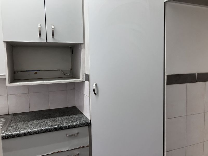 A compact kitchen area featuring built-in cabinetry, granite countertops, and a tiled backsplash, currently showing signs of wear and exposed wiring.