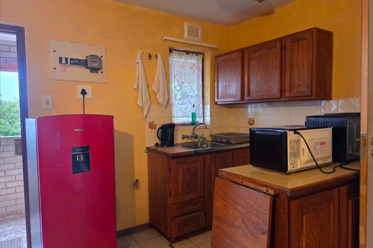 A compact kitchen featuring traditional wooden cabinetry, a stainless steel sink, and tiled backsplash, offering a functional space with potential for modern updates.