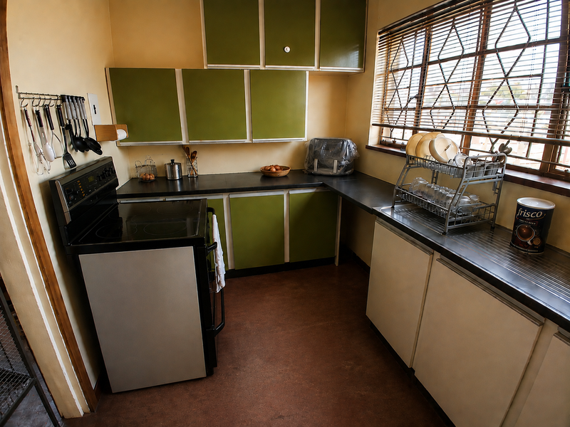 A compact kitchen featuring dated green and white cabinetry, black laminate countertops, and a freestanding electric stove with security bars on the window.