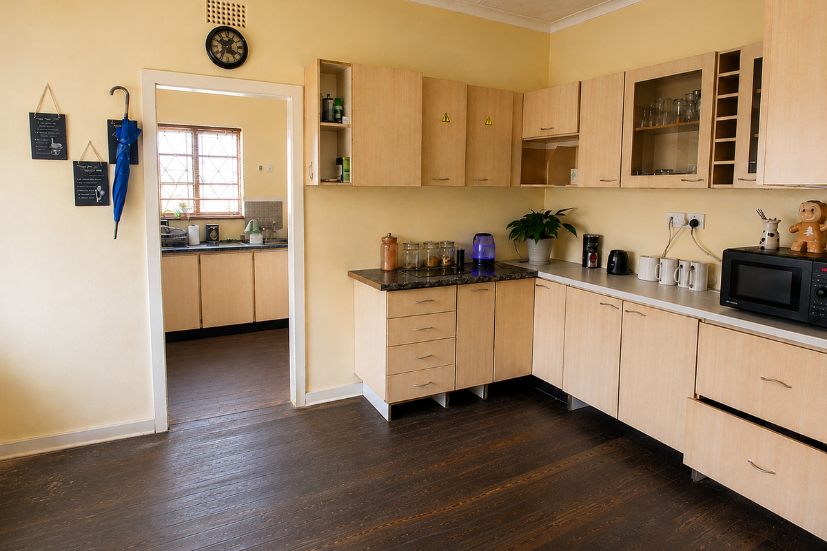 A functional kitchen featuring light wood-tone cabinetry, laminate countertops, and dark timber flooring, with an adjacent scullery area visible through the doorway.