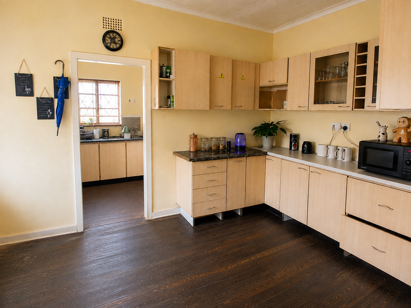 A functional kitchen featuring light wood-tone cabinetry, laminate countertops, and dark timber flooring, with an adjacent scullery area visible through the doorway.