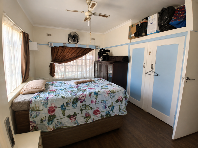 A functional bedroom featuring built-in cupboards, laminate flooring, and a ceiling fan, offering a practical layout with potential for cosmetic updates.
