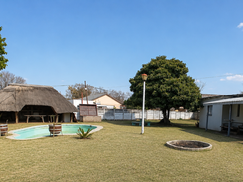 Spacious backyard featuring a swimming pool, a traditional thatch lapa, a fire pit, and established garden area enclosed by perimeter walling.
