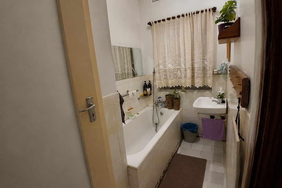 A compact bathroom featuring a built-in bathtub, wall-mounted basin, and tiled finishes, offering a functional space with potential for modernization.