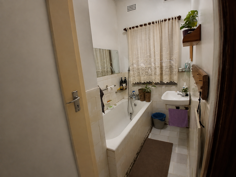 A compact bathroom featuring a built-in bathtub, wall-mounted basin, and tiled finishes, offering a functional space with potential for modernization.