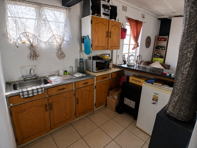 A compact kitchen featuring wooden cabinetry, a stainless steel sink, and a breakfast bar, offering a functional layout with potential for modern updates.