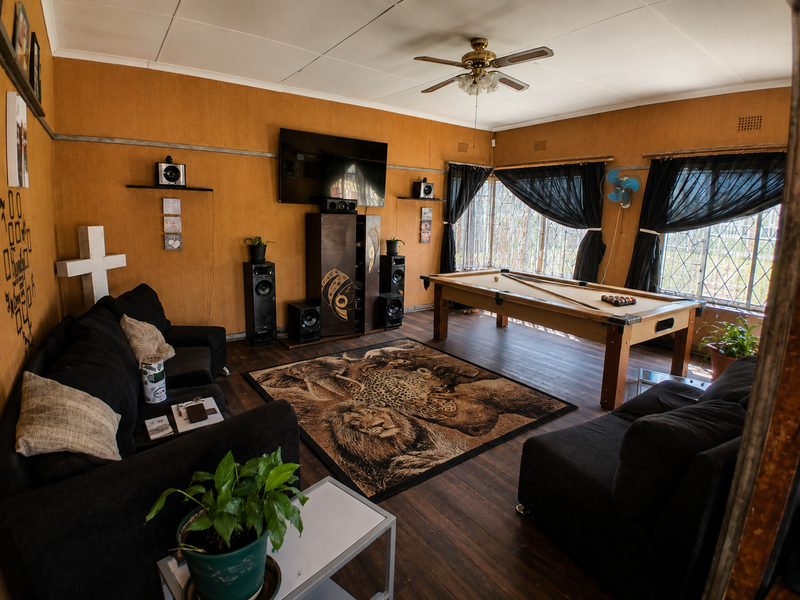 Spacious living area featuring hardwood flooring, ceiling fan, and security bars on windows, currently utilized as a lounge and games room.