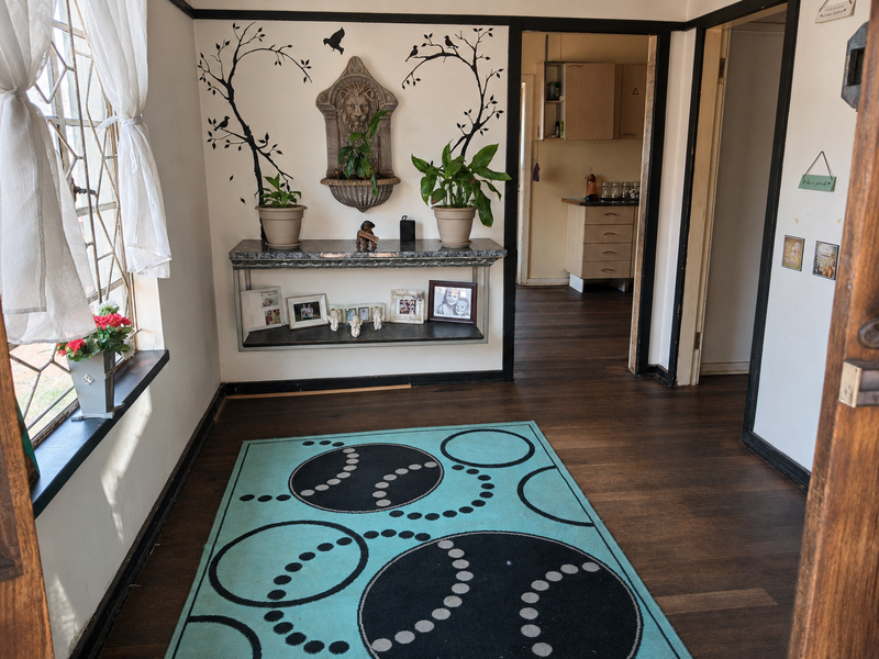 An entry area featuring dark laminate flooring, a built-in wall shelf, and a leaded glass window, leading through to the kitchen area.