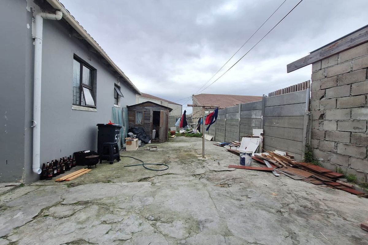 Rear exterior area featuring concrete paving, a boundary wall, and a storage shed, offering potential for landscaping and outdoor improvement.