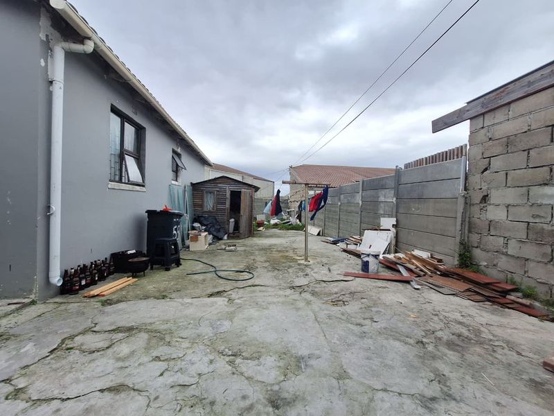 Rear exterior area featuring concrete paving, a boundary wall, and a storage shed, offering potential for landscaping and outdoor improvement.