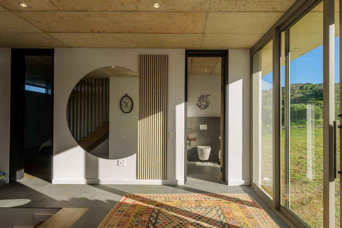 Modern living area featuring exposed concrete ceilings, large sliding glass doors providing natural light, and sleek tiled flooring with access to an adjacent bathroom.