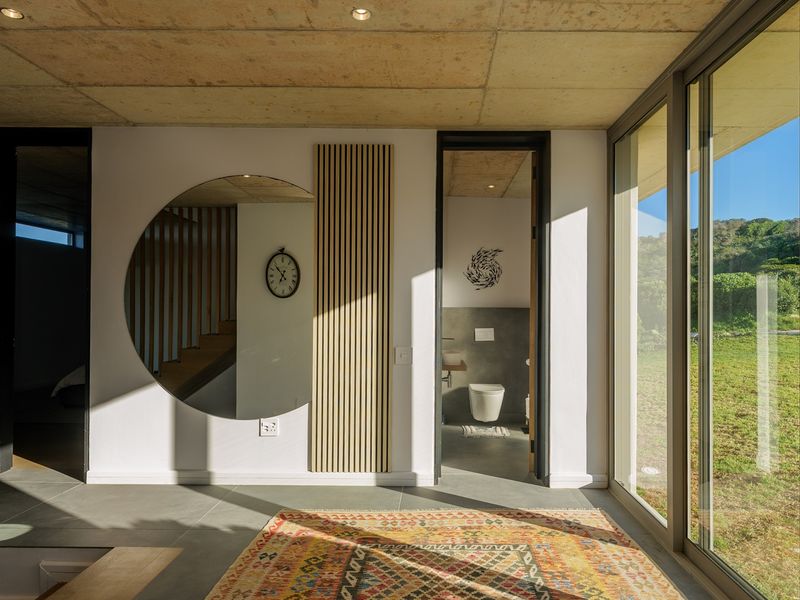 Modern living area featuring exposed concrete ceilings, large sliding glass doors providing natural light, and sleek tiled flooring with access to an adjacent bathroom.