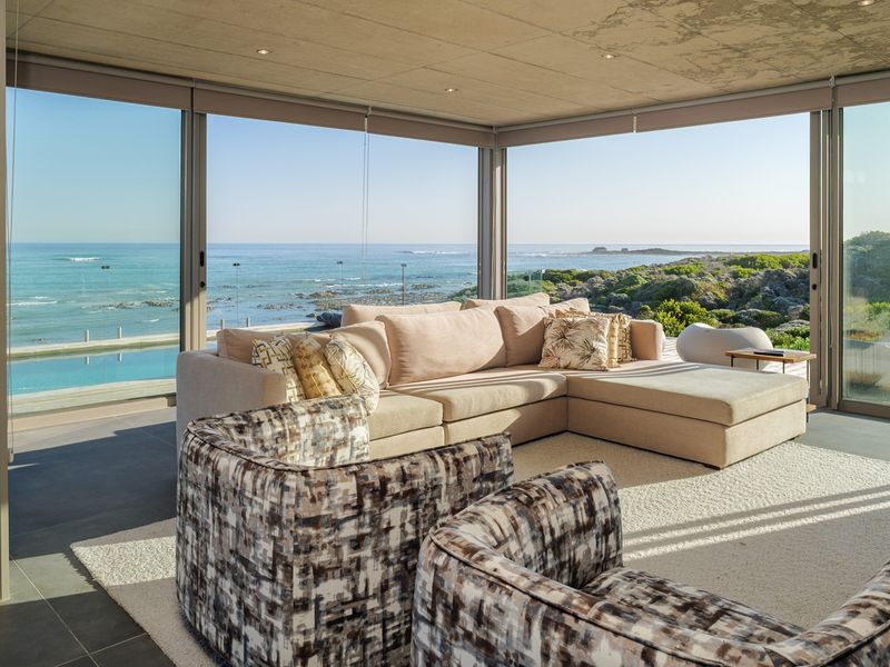Modern living area featuring expansive floor-to-ceiling glass walls with panoramic ocean views and seamless indoor-outdoor flow.